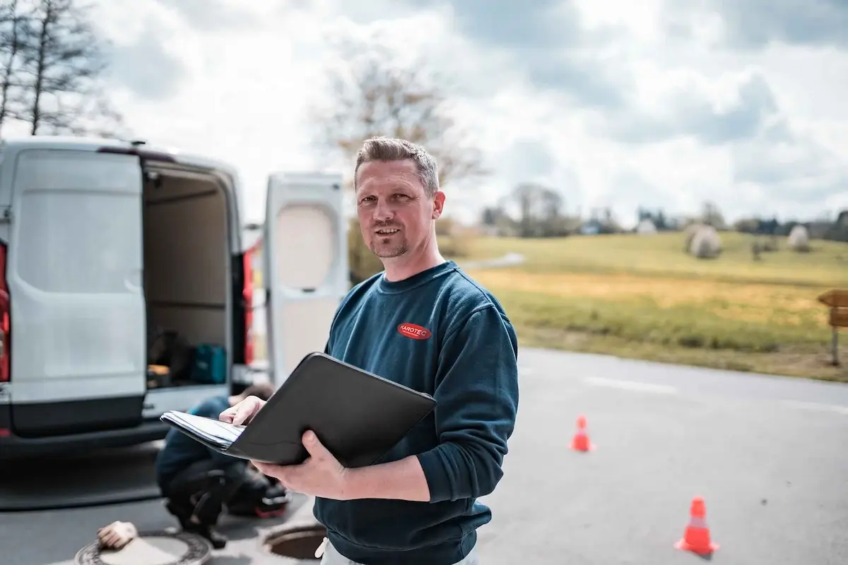 Fachmann für Kanalreinigung Achern bei der Arbeit mit Laptop und Fahrzeug im Hintergrund.